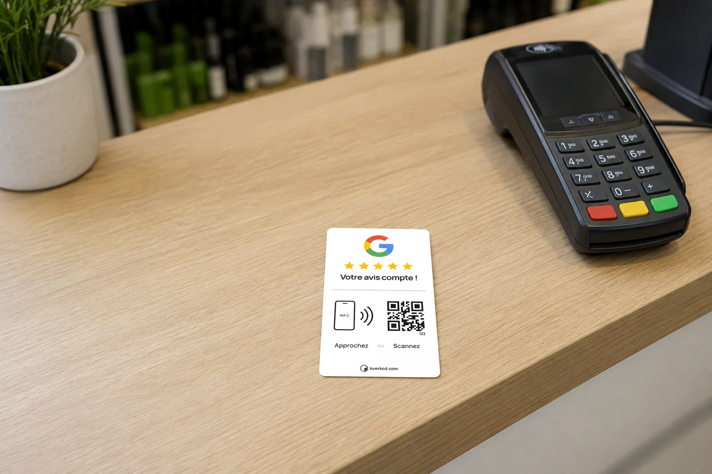 Carte Avis Google NFC/QR Kuerkod posée sur un comptoir en bois clair, juste à côté d'un terminal de paiement.